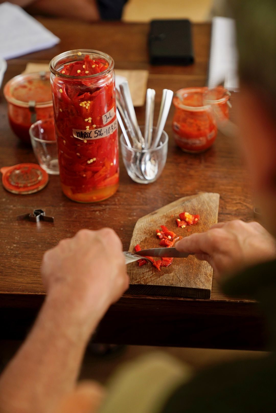 Mains qui découpent des piments rouges, bocaux de piments fermentés autour