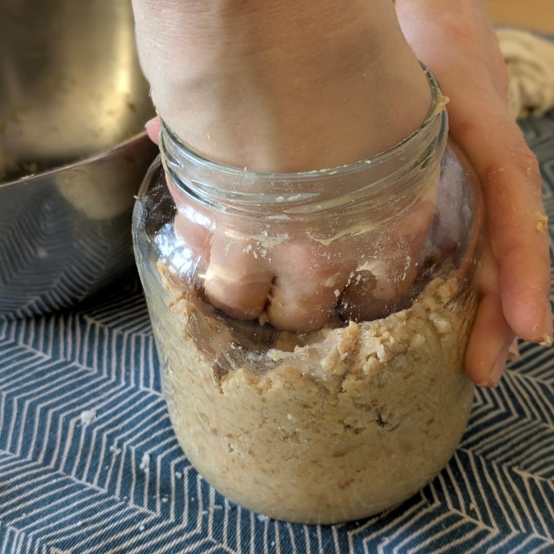 Une main tasse la pâte de miso dans un bocal