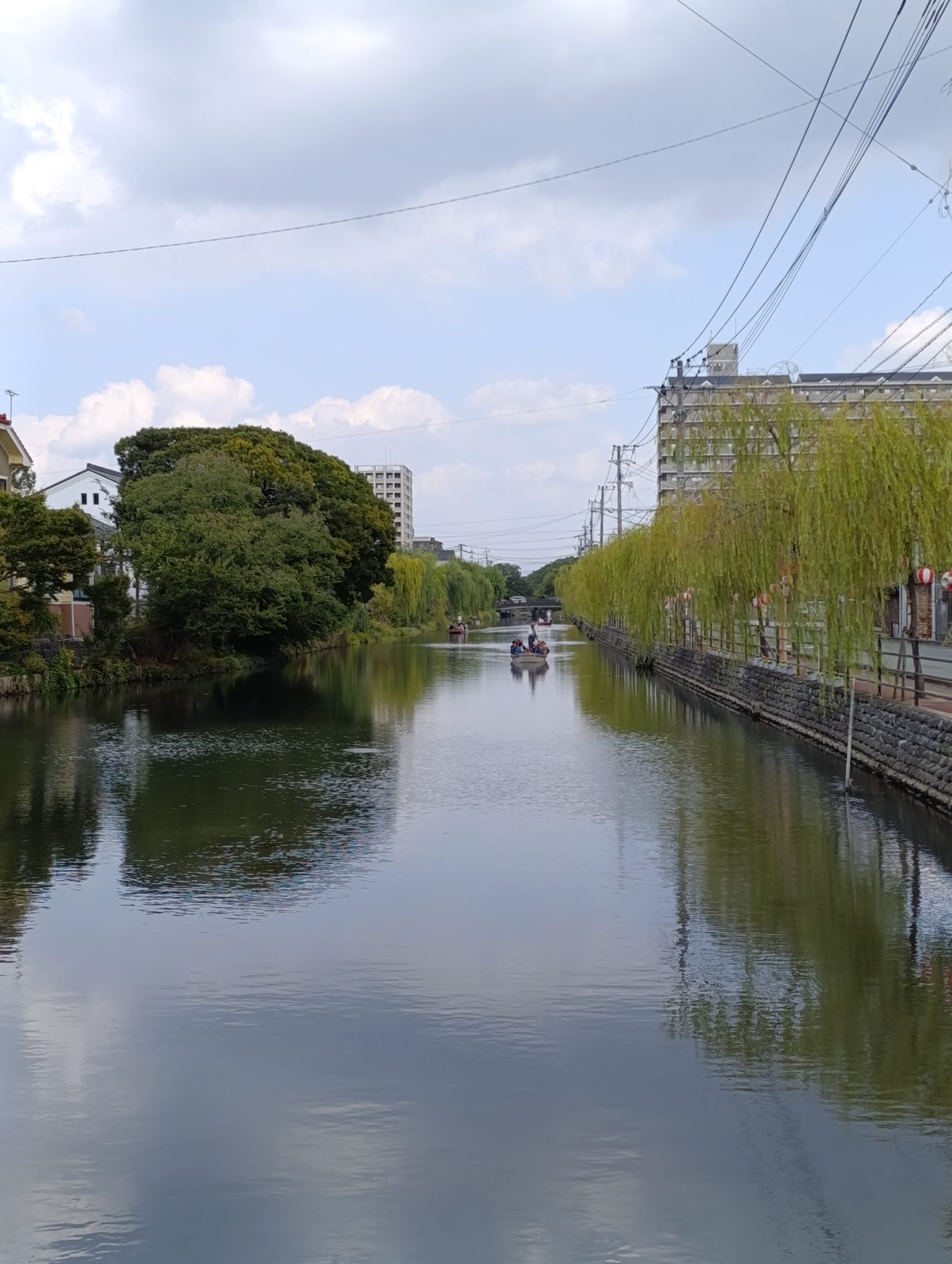 Un canal de Yanagawa bordé de saules pleureurs, avec une barque au loin