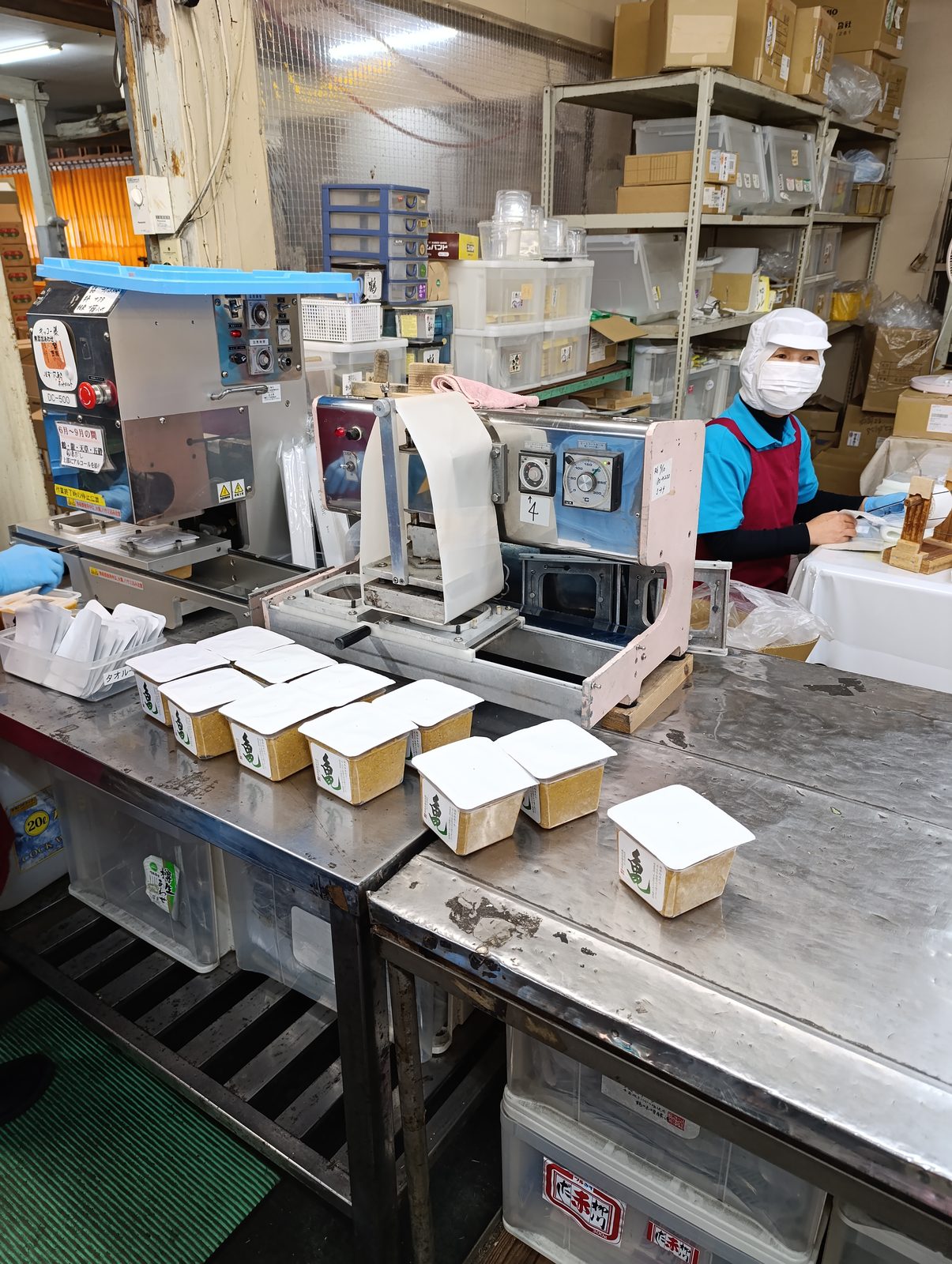 Une salariée scelle des barquettes de miso une par une sur une table en inox
