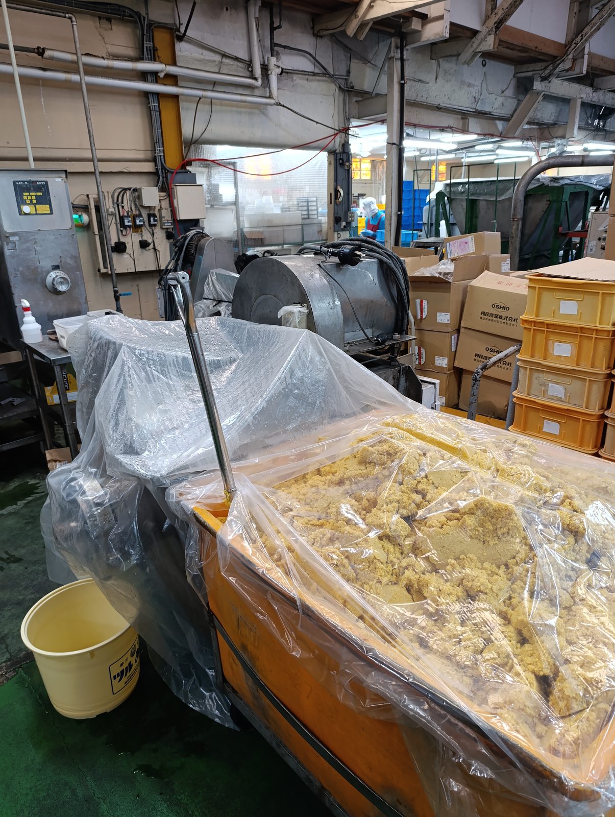 Un bac orange rempli de miso frais jaune paille en gros grumeaux, avec une pelle plantée dedans