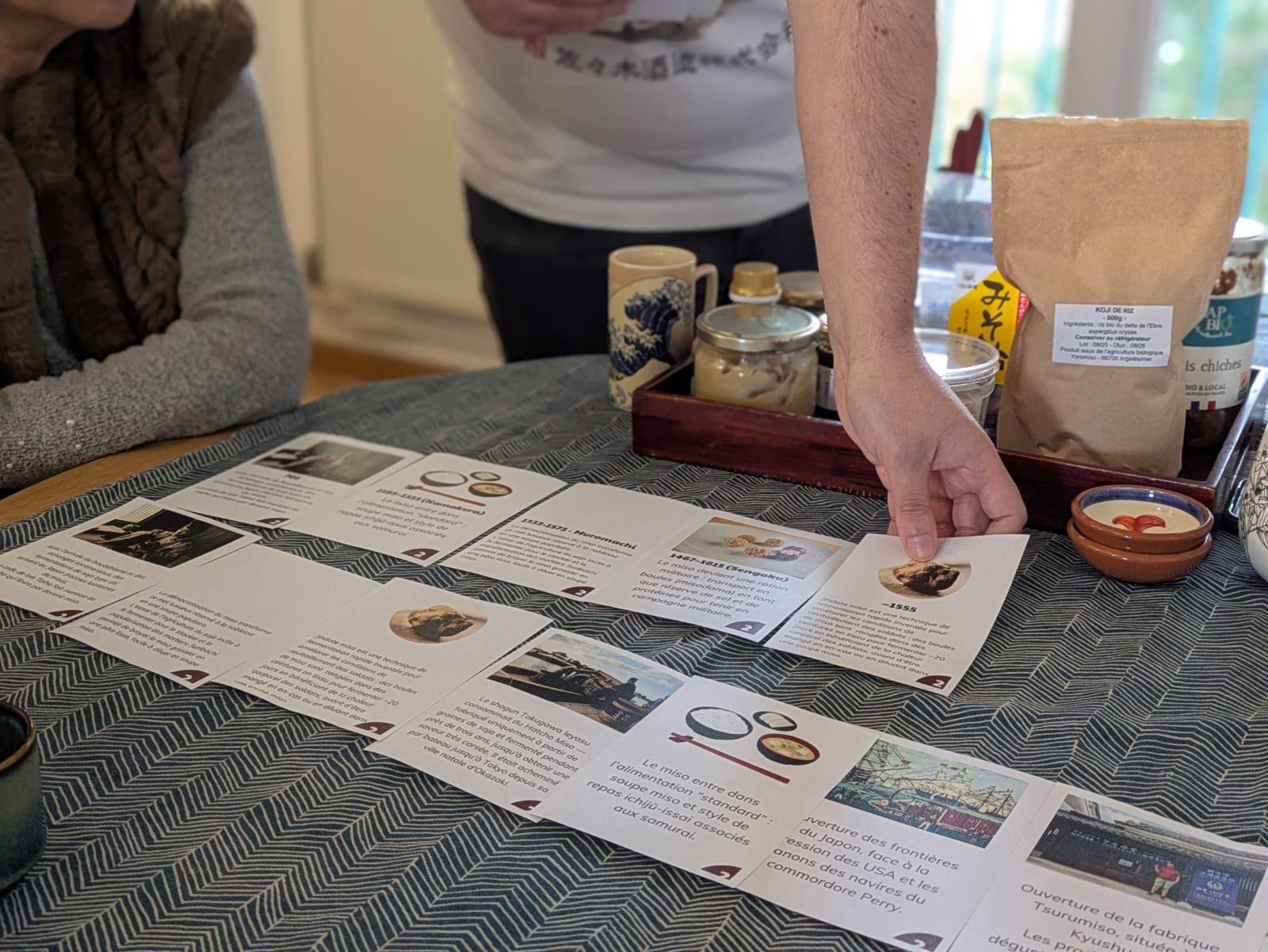 Cartes pédagogiques sur l'histoire du miso étalées sur la table d'un atelier